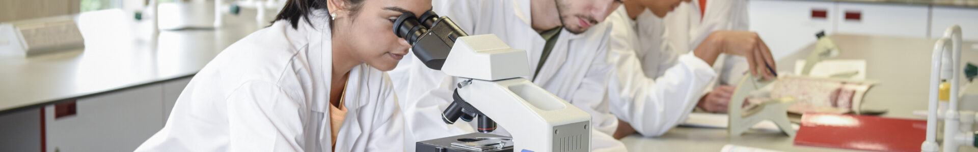 young professionals in white lab coats look at a microscope in a laboratory