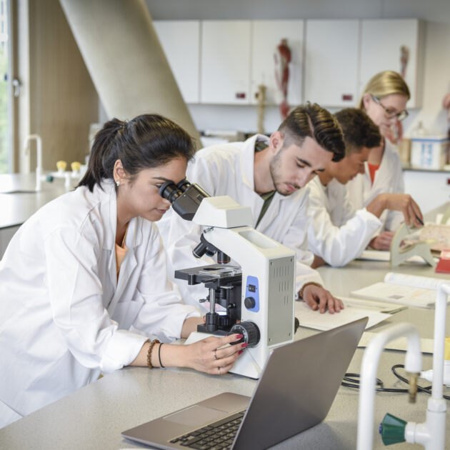 young professionals in white lab coats look at a microscope in a laboratory