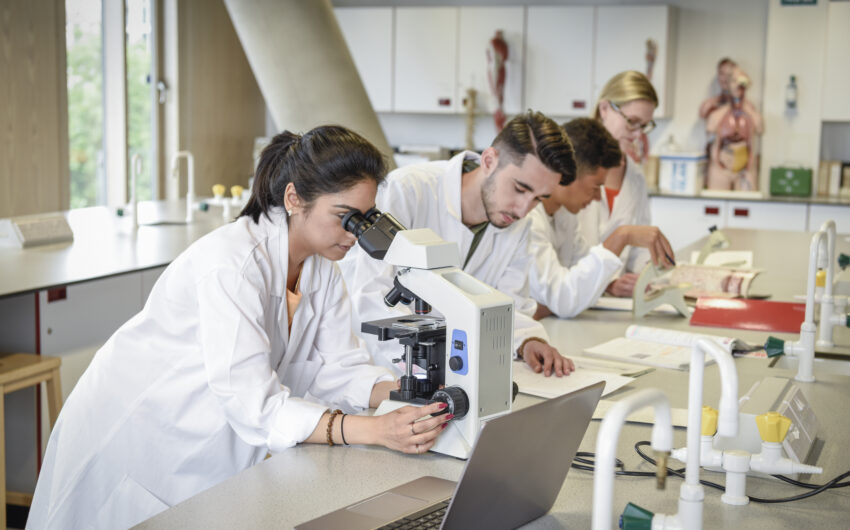 young professionals in white lab coats look at a microscope in a laboratory