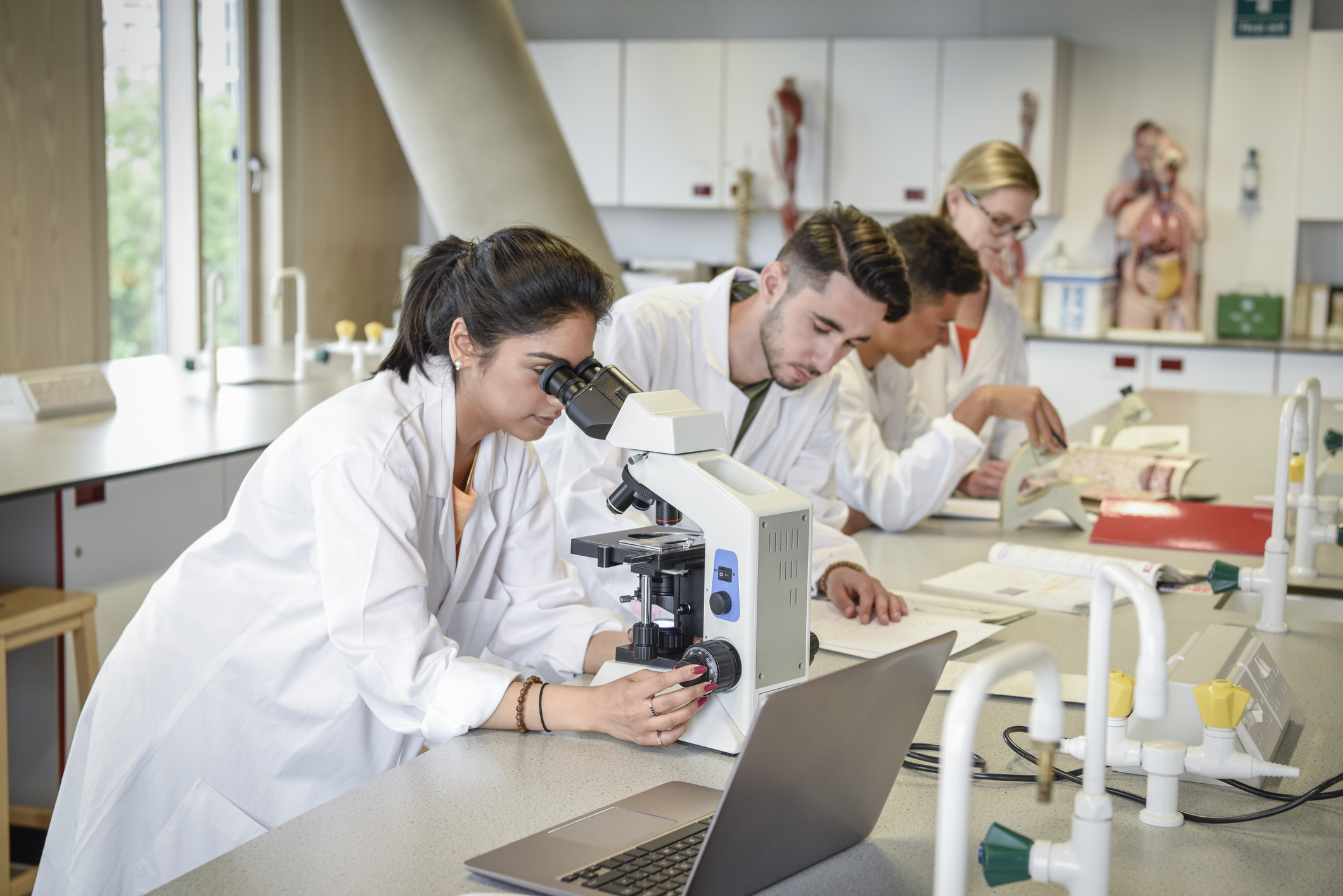 young professionals in white lab coats look at a microscope in a laboratory