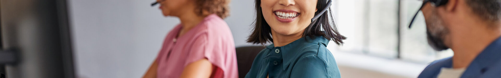 Happy customer service representative interacting with colleagues in a call center. Call center agent smiling while collaborating with support team. Young asian woman with headset talking to her supervisor while working.
