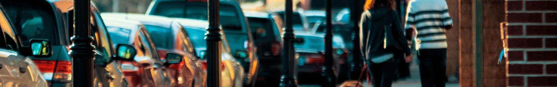 A man and a woman walk a dog down a quiet street in the morning light